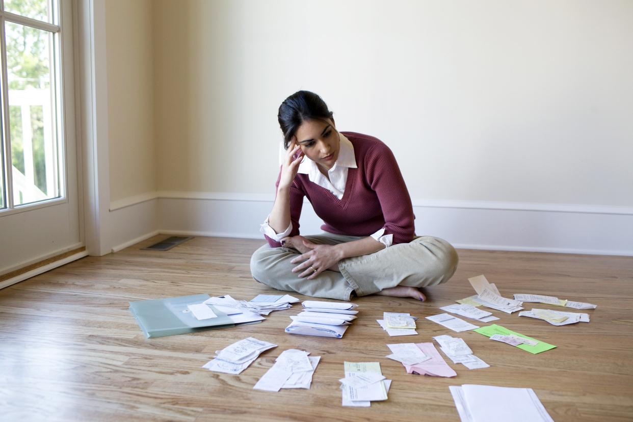 Woman on the floor surrounded by bills looking upset