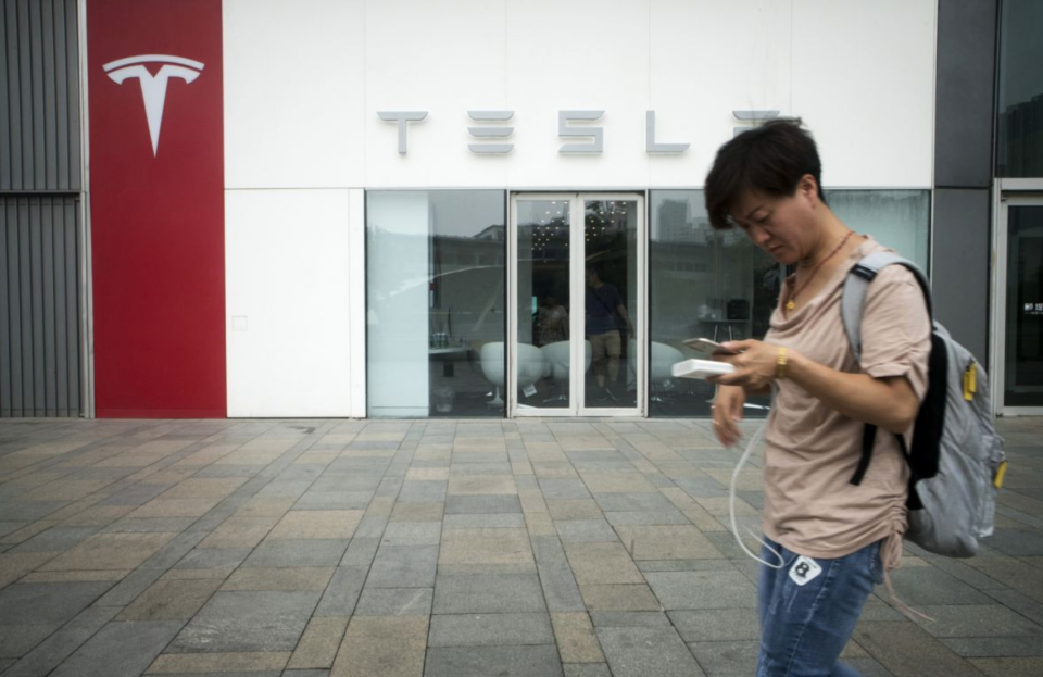 A pedestrian using a smartphone walks past a Tesla Inc. showroom in Beijing, China, on Saturday, July 7, 2018. (Photo: Giulia Marchi/Bloomberg via Getty Images)