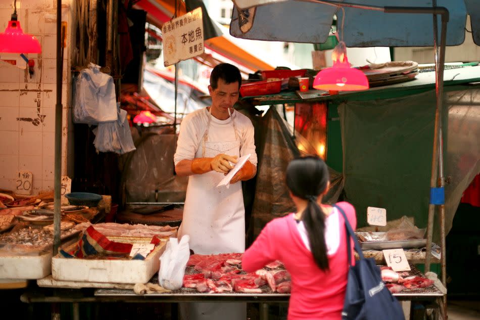 A butcher smokes a cigarette as he serves a customer from his street-side shop in Hong Kong.