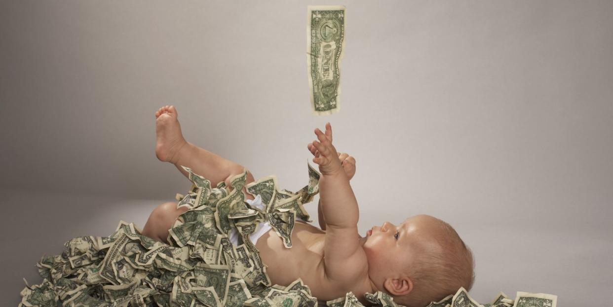 baby girl 5 months lying down covered with us dollar bills falling from above