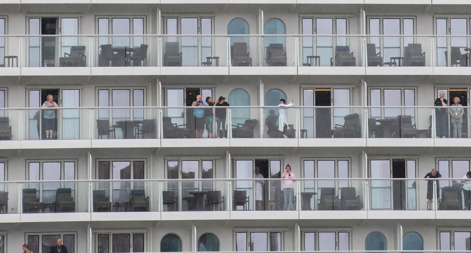 Passengers on a cruise look out over their balconies.