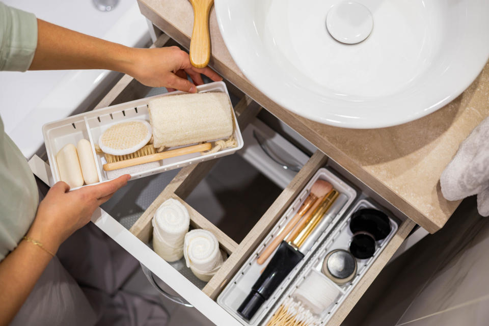 Person organizing bathroom drawer with compartments containing toiletries and grooming tools