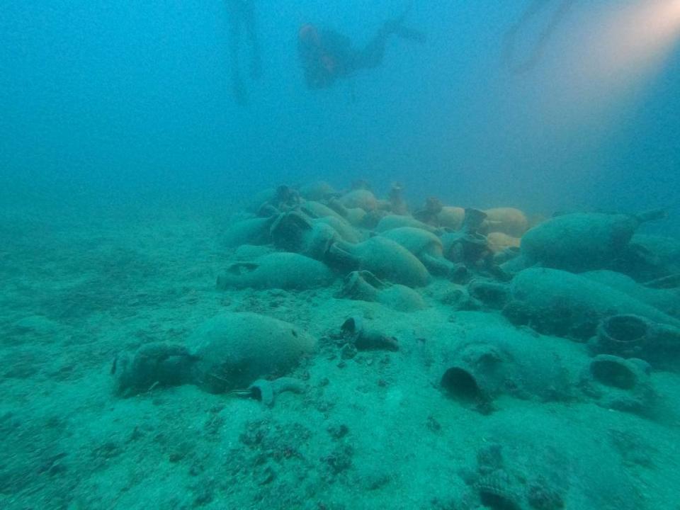 Scuba divers study the pottery cargo sitting atop the shipwreck.