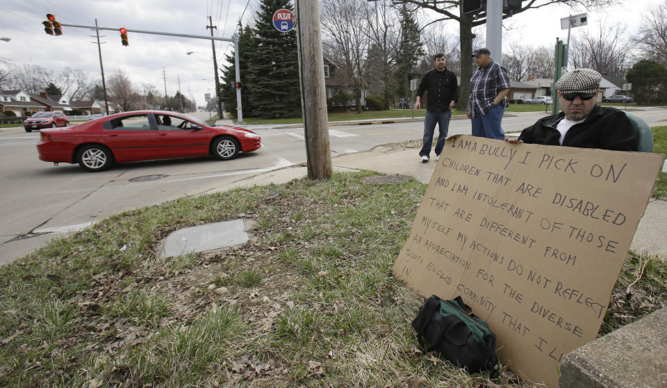 Edmond Aviv sits on a street corner holding a sign Sunday, April 13, 2014, in South Euclid, Ohio declaring he's a bully, a requirement of his sentence because he was accused of harassing a neighbor and her disabled children for the past 15 years. Municipal Court Judge Gayle Williams-Byers ordered Aviv, 62, to display the sign for five hours Sunday. It says: "I AM A BULLY! I pick on children that are disabled, and I am intolerant of those that are different from myself. My actions do not reflect an appreciation for the diverse South Euclid community that I live in." (AP Photo/Tony Dejak)