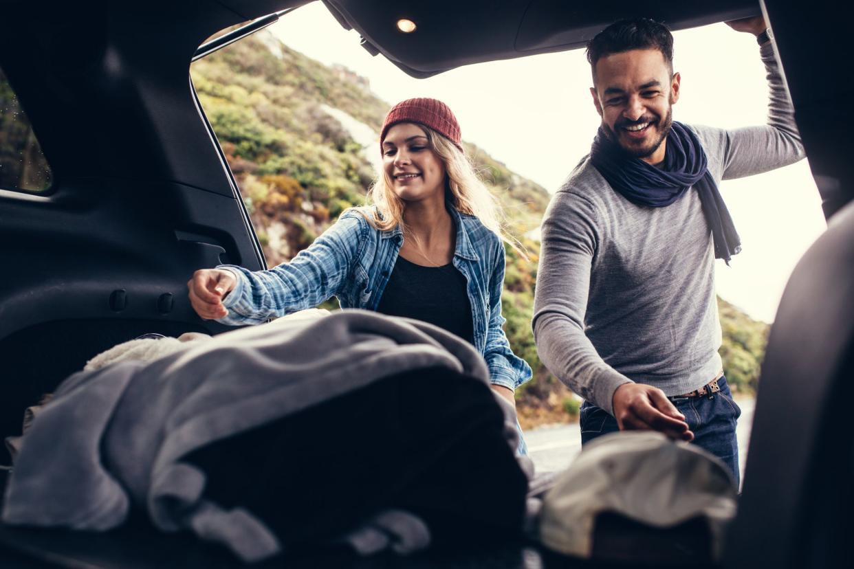 Happy couple on a vacations, taking their luggage out of car boot. Beautiful couple on a road trip.