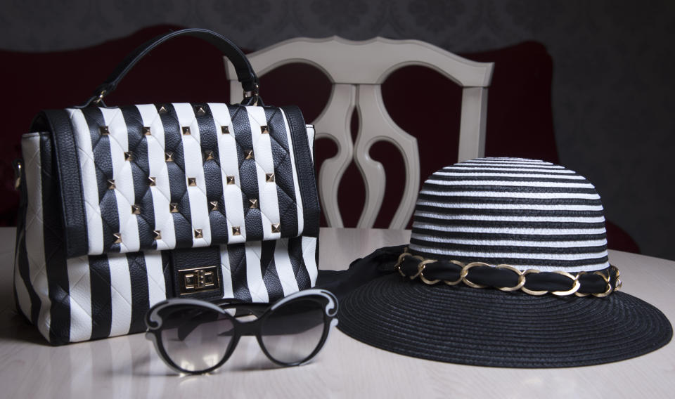 Striped women's hat, black and white purse with stripes and sunglasses on table. Modern fashion style