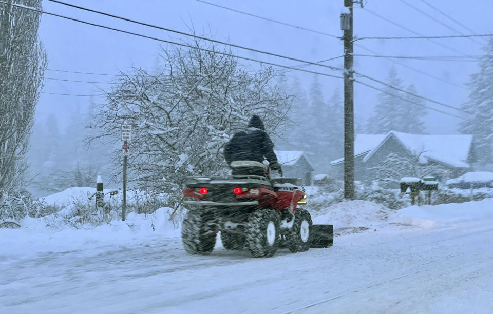 A person uses a four-wheeler to plow snow northeast of Bellingham, Wash., on Tuesday morning, Dec. 20, 2022. Heavy snow, freezing rain and sleet have disrupted travel across the Pacific Northwest, causing widespread flight cancellations and creating hazardous driving conditions. (AP Photo/Lisa Baumann)