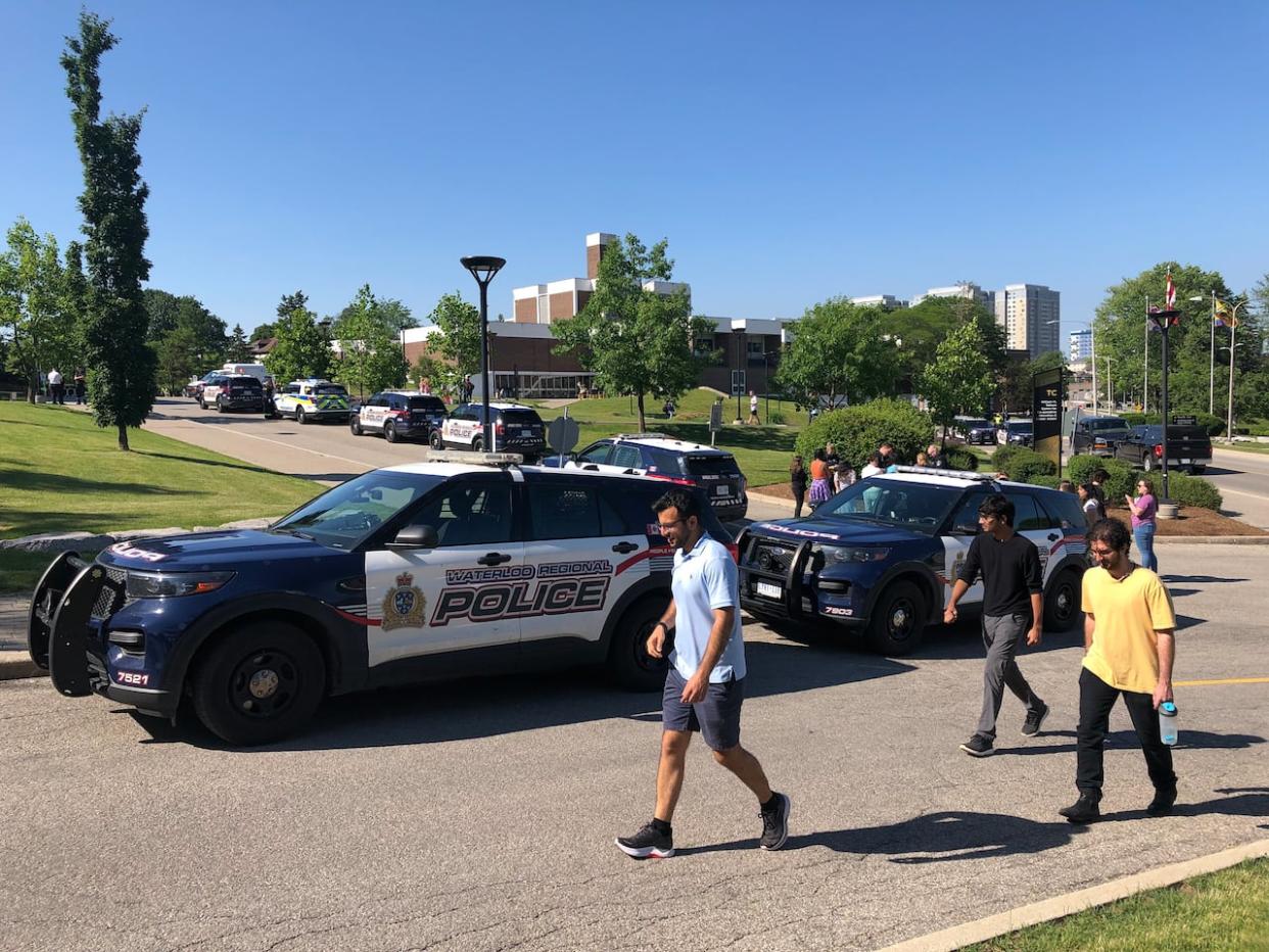 People walk past police cars at the University of Waterloo on June 28, 2023, after a triple stabbing on campus. An associate professor and two students who were in a gender-studies class were taken to hospital. (Aastha Shetty/CBC - image credit)