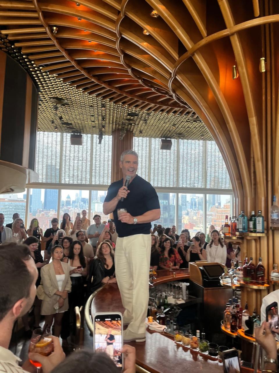 Andy Cohen standing on bar speaking to crowd at Watch What Happens Live