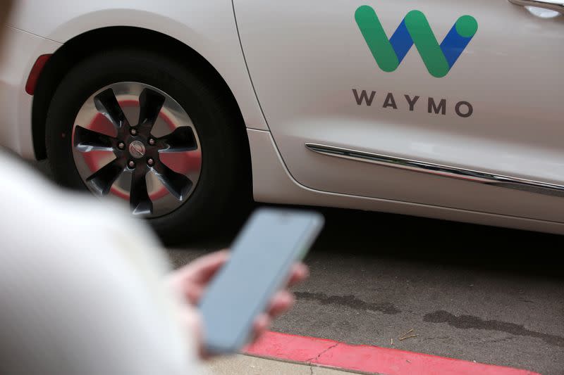 A Waymo employee hails a ride on their phone during a demonstration in Chandler, Arizona