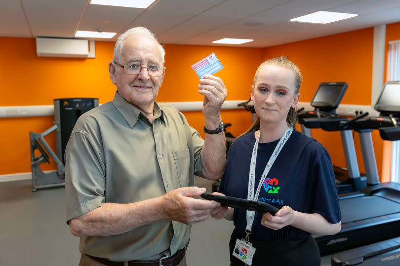 Older man holding membership pass and younger woman smiling next to him