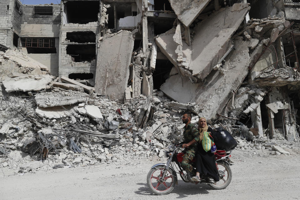 A Syrian Soldier rides his scooter as helps a woman to through a devastated part of the in the Palestinian refugee camp of Yarmouk in the Syrian capital Damascus, Syria, Saturday, Oct. 6, 2018. The camp, once home to the largest concentration of Palestinians outside the territories housing nearly 160,000 people, has been gutted by years of war. (AP Photo/Hassan Ammar)