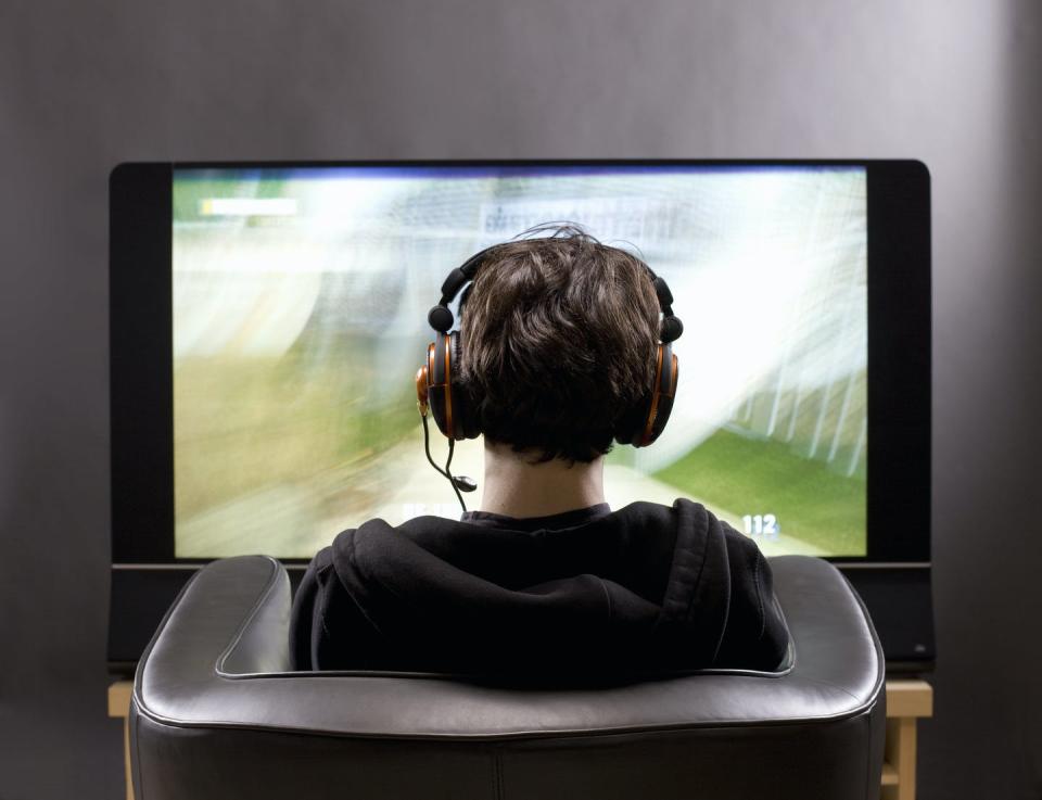 Teenage boy sits in chair playing a video game on a big flat screen.