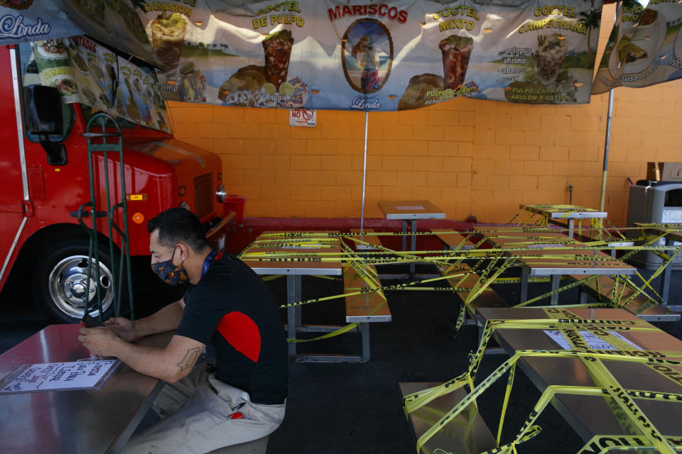 FILE - In this July 1, 2020, file photo, Abel Gomez waits for his order at Mariscos Linda food truck as dining tables are sealed off with caution tape due to the coronavirus pandemic in Los Angeles. Gov. Gavin Newsom announced a new, color-coded process Friday, Aug. 28, 2020, for reopening California businesses amid the coronovirus pandemic that is more gradual than the state's current rules to guard against loosening restrictions too soon. Counties will move through the new, four-tier system based on their number of cases and percentage of positive tests. It will rely on those two metrics to determine a tier: case rates and the percentage of positive tests. (AP Photo/Jae C. Hong, File)