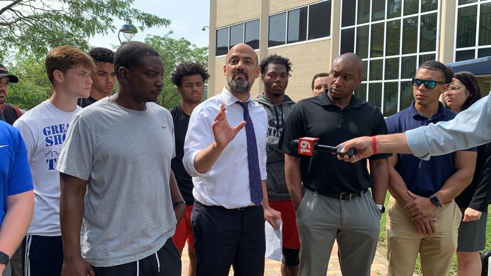 Attorney Peter Pattakos, center, stands with former McKinley High School football coach Marcus Wattley, second from right, and Wattley's assistant coaches and former players in this June 2021 photo where they explained to media members the circumstances that led up to the nontraditional lesson of asking a player to eat a pepperoni pizza while his teammates performed weighted exercises around him.
