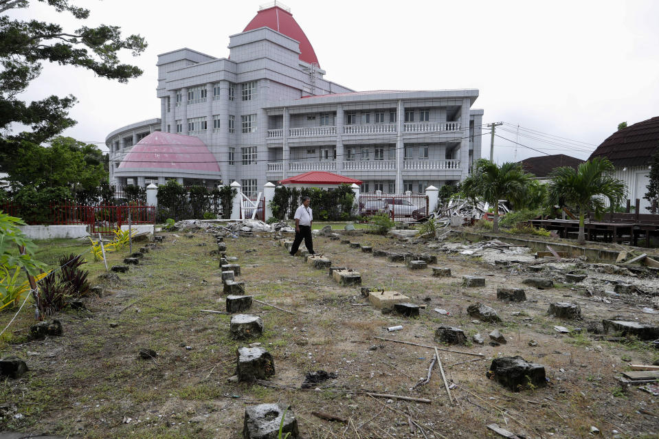 In this Wednesday, April 10, 2019, photo, a security guard walks amongst the ruins of the Tonga's historic Parliament House destroyed last year in Cyclone Gita in Nuku'alofa, Tonga. China is pouring billions of dollars in aid and low-interest loans into the South Pacific, and even in the far-flung kingdom of Tonga there are signs that a battle for power and influence among much larger nations is heating up and could exact a toll. (AP Photo/Mark Baker)