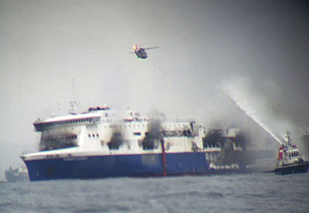 A rescue helicopter flies over the burning car ferry Norman Atlantic as a fire fighting tug boat douches the vessel in the south Adriatic sea December 28, 2014. REUTERS/Skai TV