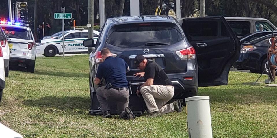 Law enforcement officials take cover outside a SunTrust Bank branch, Wednesday, Jan. 23, 2019, in Sebring, Fla. Authorities say they've arrested a man who fired shots inside the Florida bank.