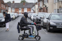 A man wearing a protective visor crosses the road on a mobility scooter, England, Monday June 29, 2020. The British government is reimposing lockdown restrictions in the central England city of Leicester after a spike in coronavirus infections, including the closure of shops that don’t sell essential goods and schools. (Joe Giddens/PA via AP)