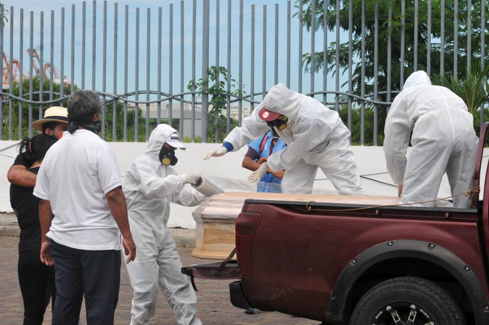 Workers wearing protective suits wrap with plastic a coffin with the remains of a person who died from the coronavirus, outside the morgue of the Hospital General Guasmo Sur in Ecuador. Source: Getty Images