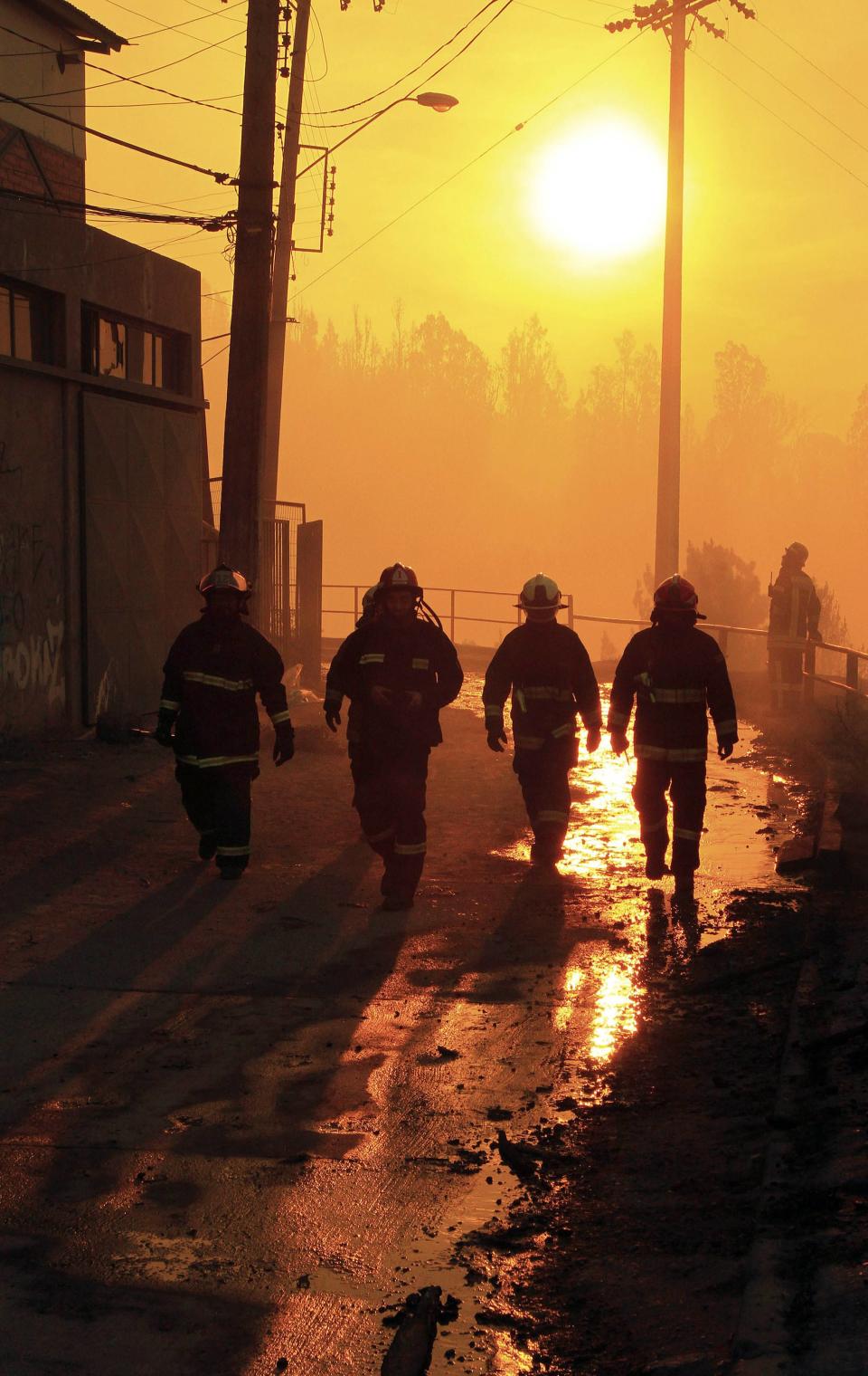 Firefighters walk past an area where a forest fire burned several neighbourhoods in the hills in Valparaiso city, northwest of Santiago, April 13, 2014. At least 11 people were killed and 500 houses destroyed over the weekend by the fire that devastated parts of the Chilean port city of Valparaiso, as authorities evacuated thousands and sent in aircraft to battle the blaze. REUTERS/Carlos Gutierrez (CHILE - Tags: SOCIETY ENVIRONMENT DISASTER)