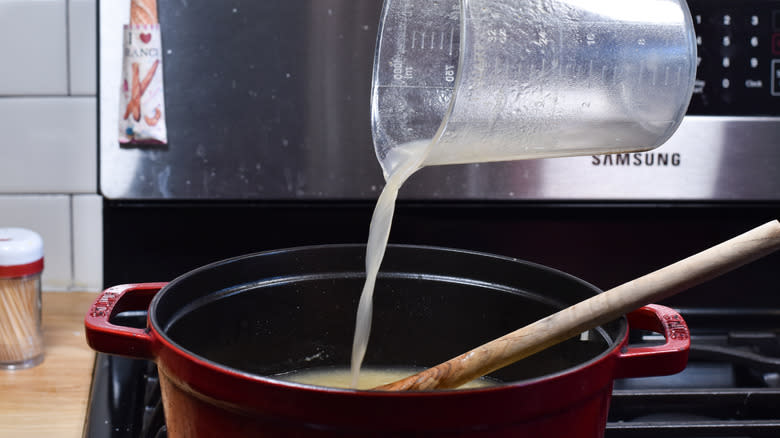 adding chicken broth to soup pot