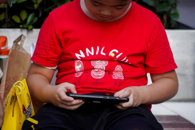 A boy plays a game on a phone on a street in Shanghai