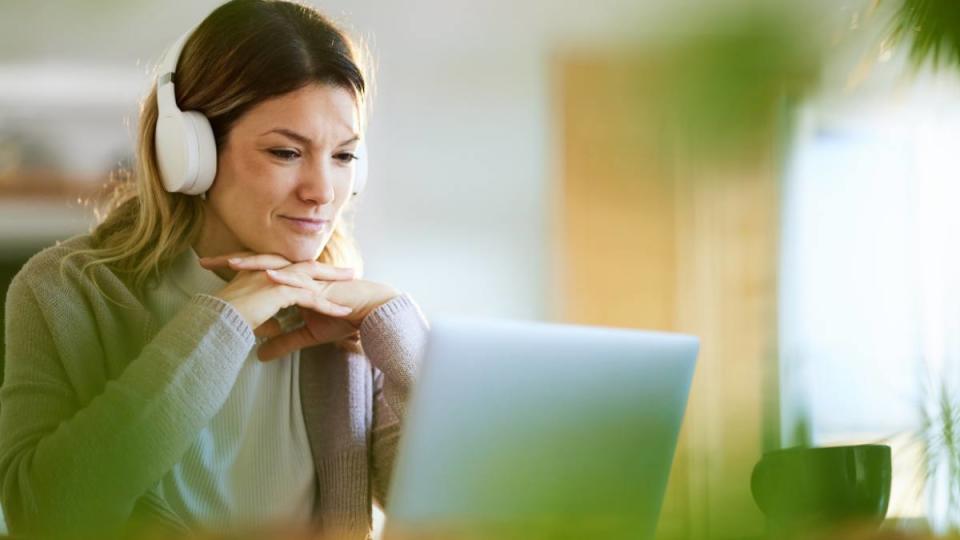 Smiling woman with headphones using laptop at home office.