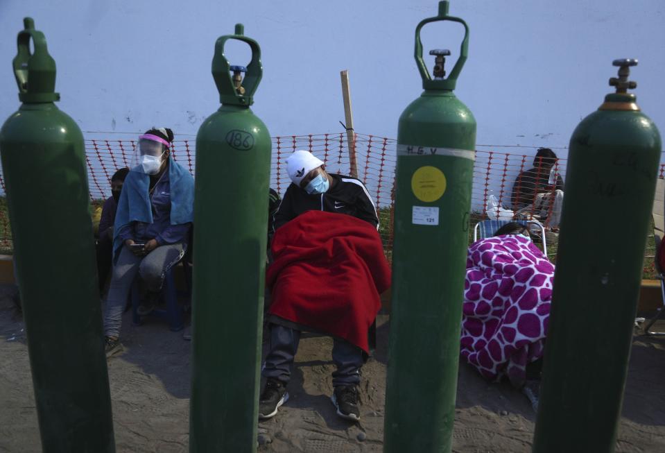 People sleep framed by their empty oxygen cylinders waiting for a shop to open to refill their tanks, in the Villa El Salvador neighborhood of Lima, early Thursday morning, Feb. 18, 2021. A crisis over the supply of medical oxygen for coronavirus patients has struck nations in Africa and Latin America, where warnings went unheeded at the start of the pandemic and doctors say the shortage has led to unnecessary deaths. (AP Photo/Martin Mejia)