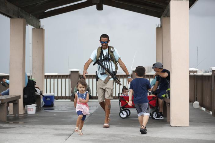 FILE - Michael Taylor, also known as "The Armed Fisherman", walks along Pier 60 in Clearwater Beach, Fla., with his 2-year-old daughter Ocean and his assault rifle and fishing gear, on July 3, 2021. Advocates say permitless carry makes people safer. Opponents say it makes it more dangerous for ordinary people, and for police officers. (Octavio Jones/Tampa Bay Times via AP, File)