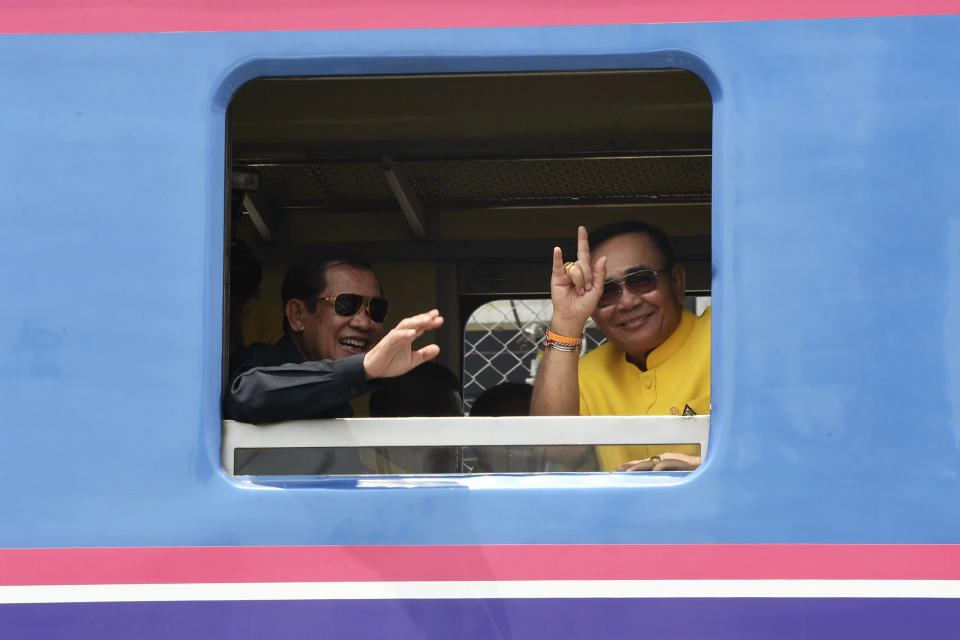In this photo released by the Government Spokesman's Office, Cambodian's Prime Minister Hun Sen, left, and Thailand's Prime Minister Prayuth Chan-ocha wave from a window on a train at the Thai-Cambodian border town of Aranyaprathet, Thailand, Monday, April 22, 2019. The leaders have met to mark the ceremonial reopening of a rail link that will restore rail service between the two countries after more than four decades. (Government Spokesman Office via AP)