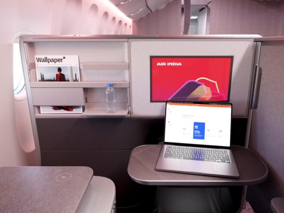 The inside of business class with the door closed, the TV on, and a laptop on the tray table.