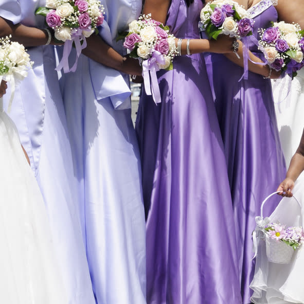 A group of people in lavender bridesmaid dresses holding bouquets. One person holds a flower basket. Names of the individuals are not known