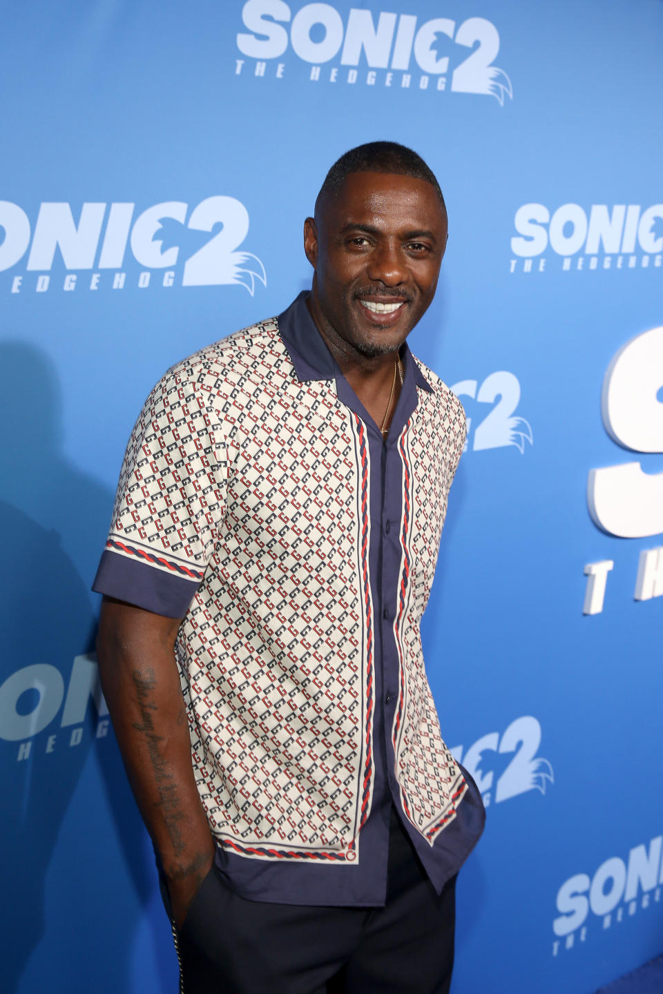 Elba in a short sleeved button-down smiling at an event