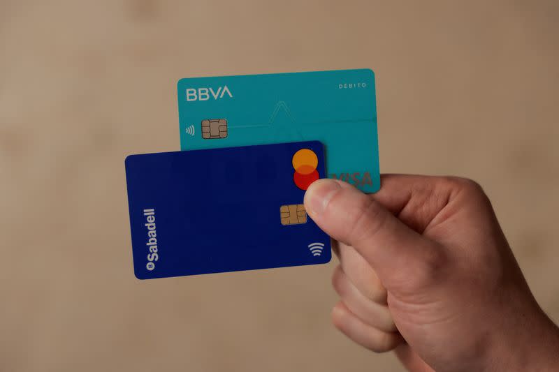 FILE PHOTO: A man shows his debit cards of BBVA and Sabadell banks, in Ronda