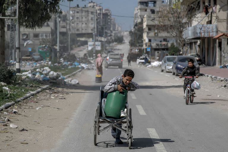 Un niño palestino transporta un contenedor de agua en silla de ruedas por una calle de la Ciudad de Gaza el 3 de marzo de 2024, en medio del conflicto en curso entre Israel y Hamas.