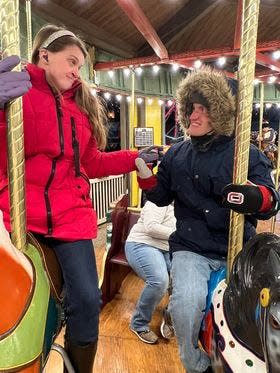Kaylee Arthurs, who is blind and deaf, reaches out to Alec Worth, who is autistic, while they ride the merry-go-round at Christmas in the Park in New Philadelphia's Tuscora Park. Her mother captured the moment in a photo that shows how Worth makes sure she is OK, and how she makes certain where he is by reaching out to him.