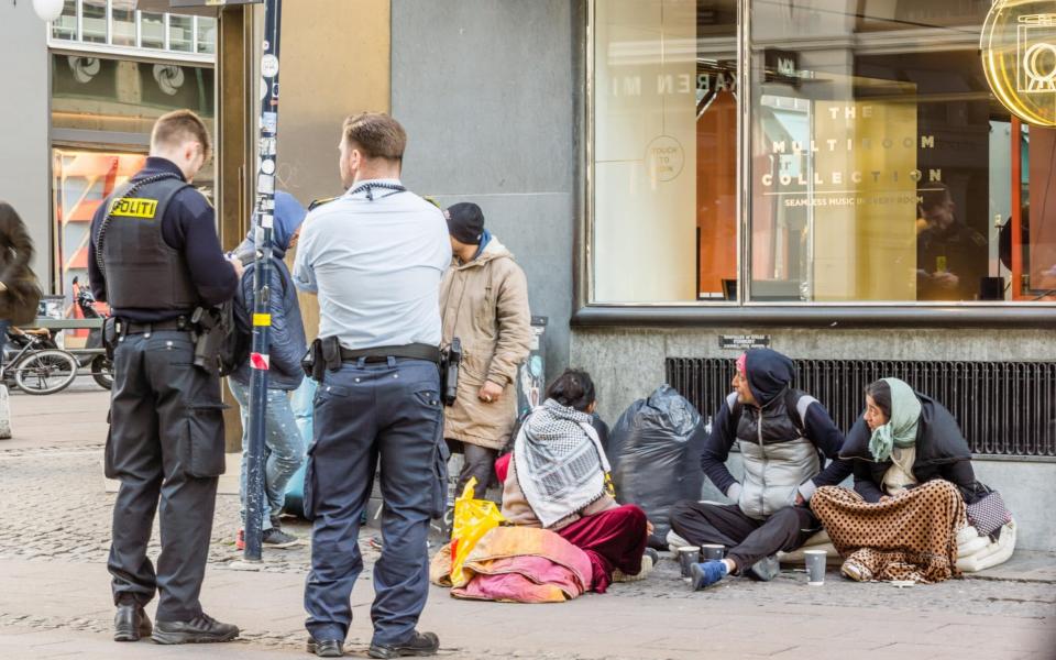 Two policemen looking at the documents of some immigrants, who are sitting on the street