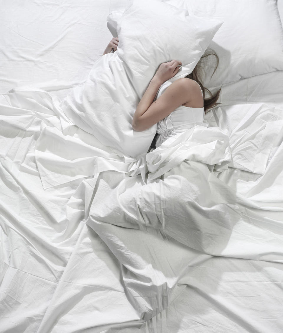 A woman laying in bed completely covered with a pillow over her face