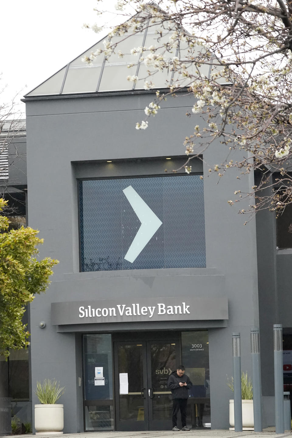 A person stands outside of an entrance to Silicon Valley Bank in Santa Clara, Calif., Friday, March 10, 2023.The Federal Deposit Insurance Corporation is seizing the assets of Silicon Valley Bank, marking the largest bank failure since Washington Mutual during the height of the 2008 financial crisis. The FDIC ordered the closure of Silicon Valley Bank and immediately took position of all deposits at the bank Friday. (AP Photo/Jeff Chiu)