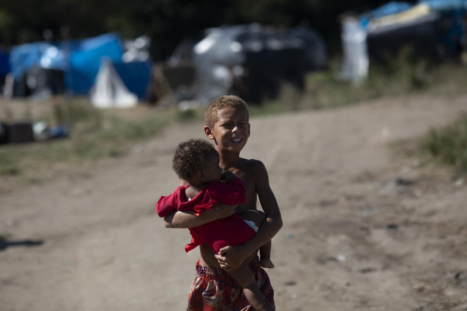 A boy holds a baby during an eviction from land designated for a Petrobras refinery, at a settlement coined the "First of May Refugee Camp," named for the date people moved in setting up tents and shacks, in Itaguai, Rio de Janeiro state, Brazil, Thursday, July 1, 2021, amid the new coronavirus pandemic. (AP Photo/Silvia Izquierdo)