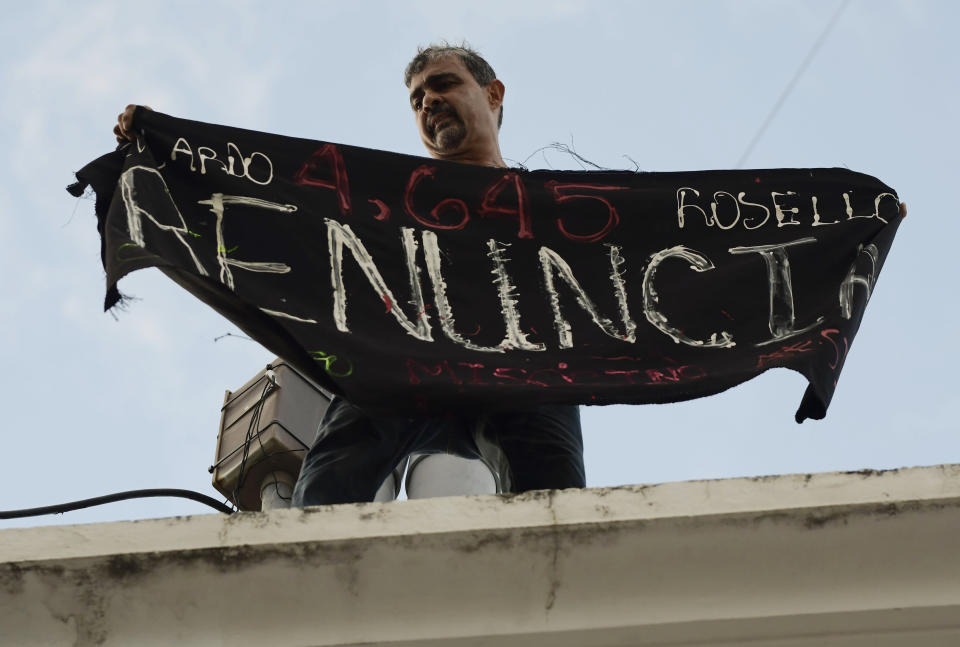 Activist Alberto de Jesús Mercado, better known has Tito Kayak, holds a banner that reads in Spanish "Resign" as he stands on top of a police headquarters across the street from La Fortaleza governor's residence during a protest in San Juan, Puerto Rico, Sunday, July 14, 2019. Protesters are demanding Gov. Ricardo Rosselló step down for his involvement in a private chat in which he used profanities to describe an ex-New York City councilwoman and a federal control board overseeing the island's finance. (AP Photo/Carlos Giusti)