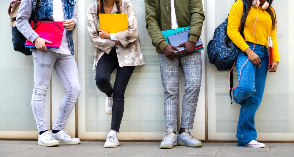 Group of multiracial teenage college students ready to go back to school standing against blue background wall