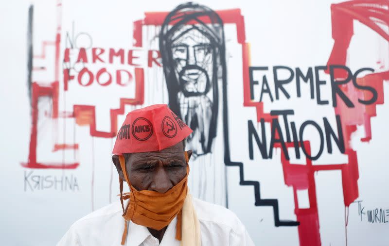 A farmer sits in front of a graffiti during a protest against new farm laws in Mumbai