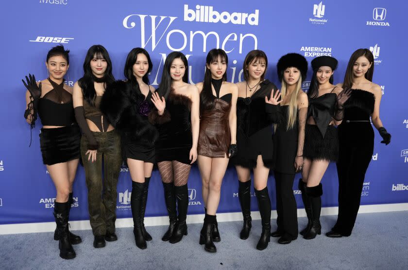 A group of nine women in black stand and post in front of a blue backdrop