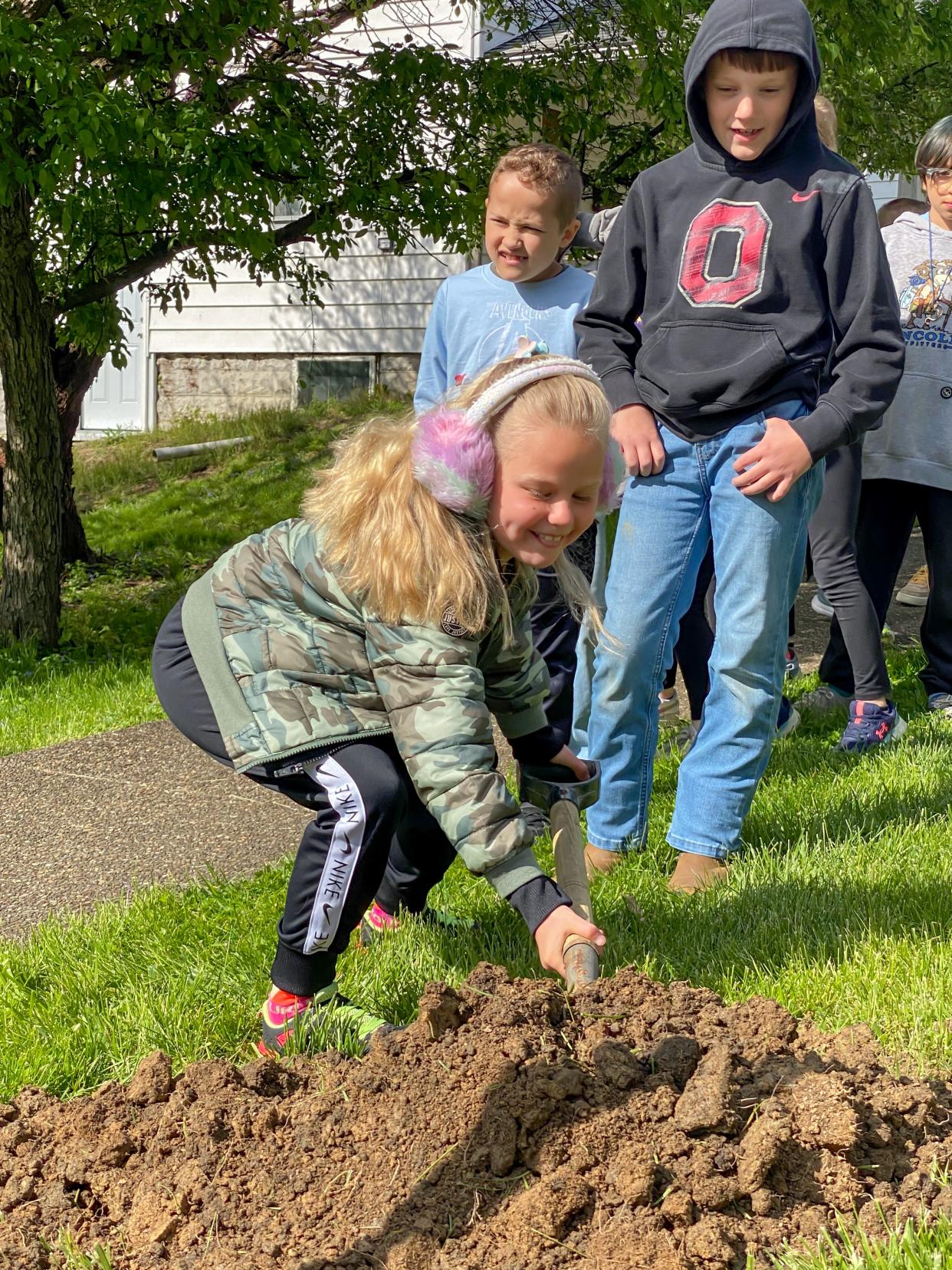 Second-grade students from New Concord Elementary take turns shoveling dirt around the base of a newly planted Japanese Zelkova tree.