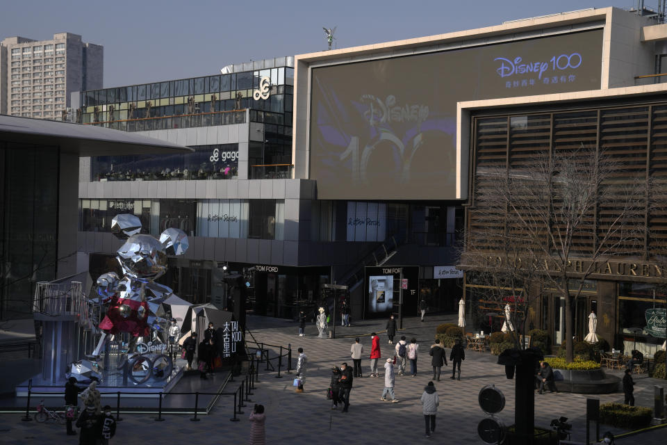 Visitors wearing face masks tour past an outdoor shopping center displaying a Mickey Mouse statue commemorating the Disney 100th anniversary in Beijing, Thursday, Jan. 5, 2023. As COVID-19 rips through China, other countries and the WHO are calling on its government to share more comprehensive data on the outbreak, with some even saying many of the numbers it is reporting are meaningless. (AP Photo/Andy Wong)
