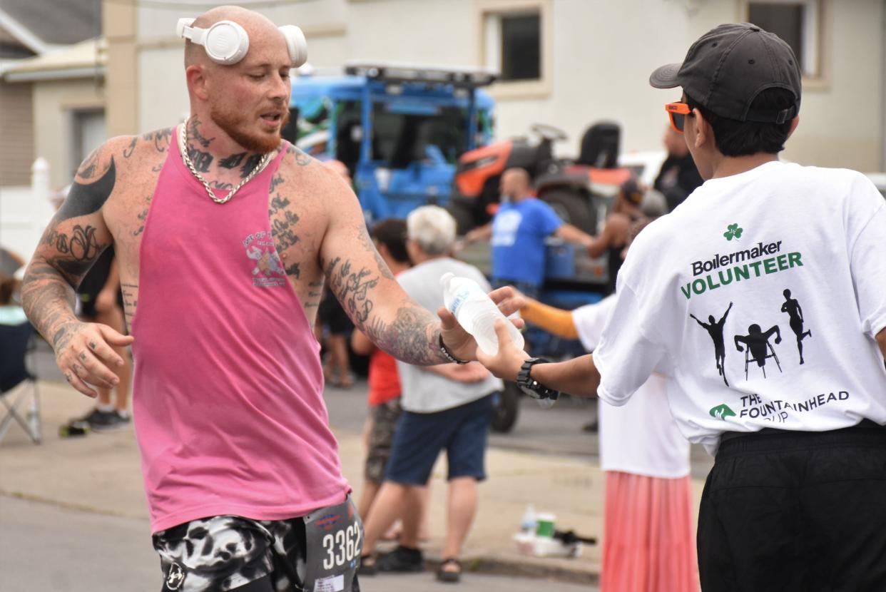 Sean Brewer (left) of Mohawk accepts a bottle of water from Boilermaker Road Race volunteer at the turn onto Whitesboro Street in Utica, New York, Sunday, July  9, 2023.  "I ran the race for (my dad in hospice care)," Brewer said, "because it was his favorite road race and he was an avid runner."