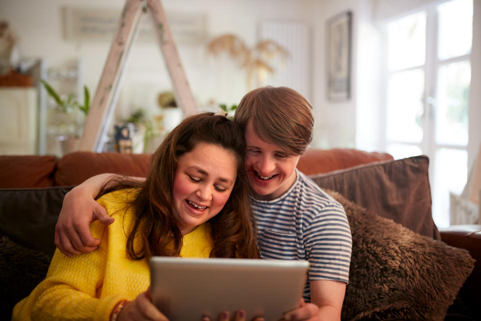 Loving Young Downs Syndrome Couple Sitting On Sofa Using Digital Tablet At Home