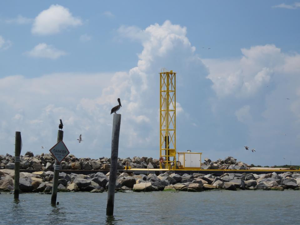 Pelicans sit on poles near a barge loaded with rocks to armor the edges of a Louisiana barrier island on a Louisiana barrier island on Wednesday, July 28, 2021. Contractors are at work on a $102 million Louisiana Coastal Restoration and Protection Authority project to add about 400 acres of beach, dune and marshland to Grand Terre Island. Weather permitting, they hope to finish in November. (AP Photo/Janet McConnaughey)